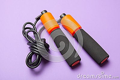 Jump rope. Fun exercises for body health. Orange rope with black cord. Violet background Stock Photo