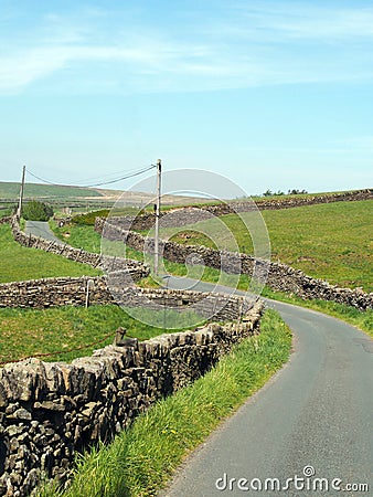 junction on a winding narrow country lane bordered by dry stone walls in hilly yorkshire dales countryside with blue summer sky Stock Photo