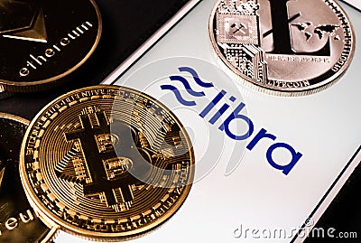 Libra the Facebook cryptocurrency logo on mobile phone screen and real coins of other crypto such as Bitcoin next to it Editorial Stock Photo