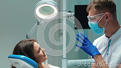 Junge, gut aussehende Zahnärztin in medizinischen blauen Handschuhen , Masken und Brillen, die mit einer schönen Patientin über d stock video Junge, gut aussehende Zahnärztin in medizinischen blauen Handschuhen , Masken und Brillen, die mit einer schönen Patientin über d stock video