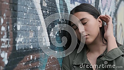 Junge schöne Mädchenstellung nahe der Wand mit Graffiti und Aufstellung, die Kamera mit einer Hand betrachtend durch ihr Haar stock video footage Junge schöne Mädchenstellung nahe der Wand mit Graffiti und Aufstellung, die Kamera mit einer Hand betrachtend durch ihr Haar stock video footage