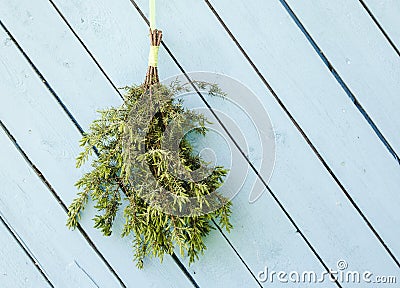 Juniper sauna whisk broom also known as vasta, vihta or venik hanging and drying on the wall, blue wooden background. Stock Photo