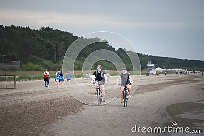 JURMALA, RIGA - AUGUST 25, 2023: Selective blur on two men, friends, biking and riding together bicycles on a beach in Jurmala Editorial Stock Photo