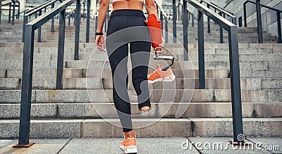 Just do it. Back view of disabled women in sports clothing holding her leg prosthesis while standing on stairs outdoors Stock Photo
