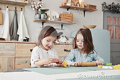 Just having free time. Two kids playing with yellow and orange toys in the white kitchen Stock Photo
