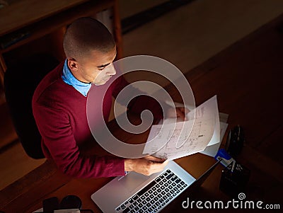 Just a little late night reading. High angle shot of a young man reading paperwork while working late in the office. Stock Photo