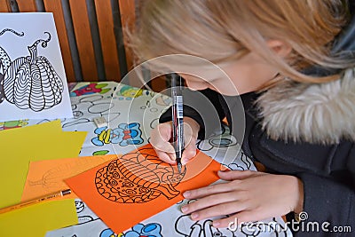 A girl draws a pumpkin with a marker on colored paper. Children`s master class in the open air Editorial Stock Photo