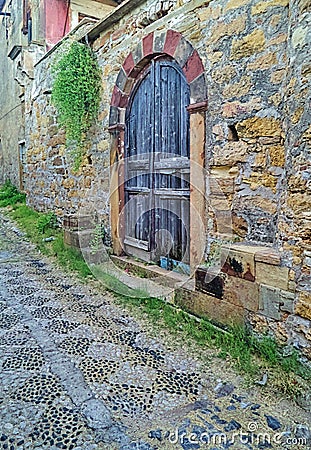 Rustic arched wooden door on stone wall and stone paved alley with shapes Stock Photo