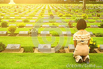 Asian woman sitting in front of black gravestone at graveyard with sunlight flare Editorial Stock Photo
