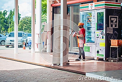 KANCHANABURI, THAILAND - OCTOBER 4,2020 : Unidentified Asian woman wear hat, mask and apron buys drinks and snacks from 7-Eleven Editorial Stock Photo