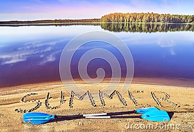 Kayak paddles laying on the lake beach near the word summer written on the sand Stock Photo