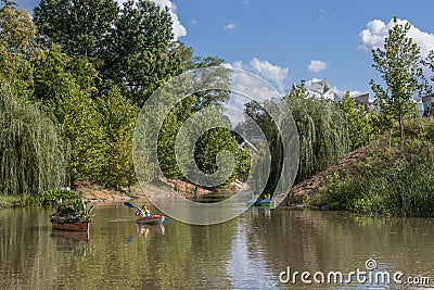 Kayaker paddles past canoe filled with plants on river in Gathering Place public park with paddle boaters and Editorial Stock Photo
