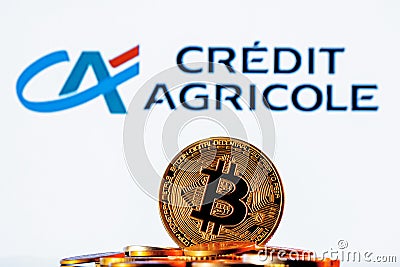 Golden bitcoin in a pile of coins on the background of Credit Agricole bank logo Editorial Stock Photo