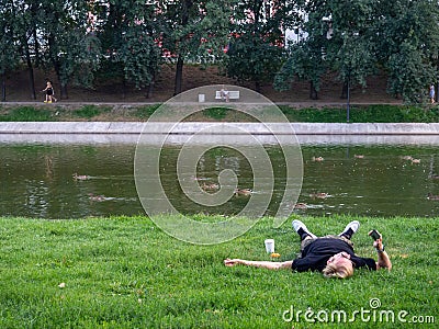 Kazan, Russia. 20.08.2021. A man is lying on the lawn near the lake with a phone Editorial Stock Photo