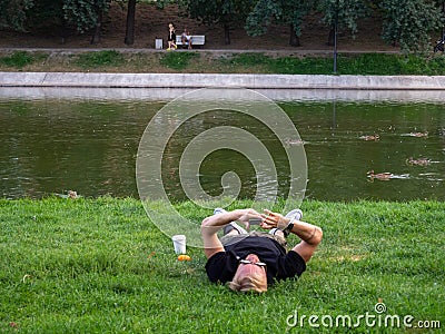 Kazan, Russia. 20.08.2021 A man is lying on the lawn near the lake with a phone Editorial Stock Photo