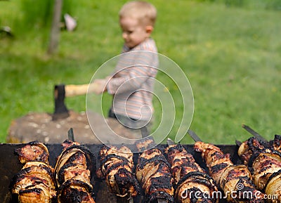 Kebabs grilling on a BBQ as a small boy chops wood Stock Photo