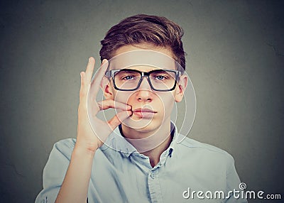 Keep a secret, young man zipping his mouth shut. Quiet concept Stock Photo