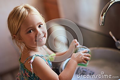 Keeping things clean. Portrait of a little girl washing dishes at home. Stock Photo