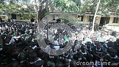 KENYA, KISUMU - MAY 23, 2017: Big crowd of African children in uniform sitting on a ground outside near school. Editorial Stock Photo