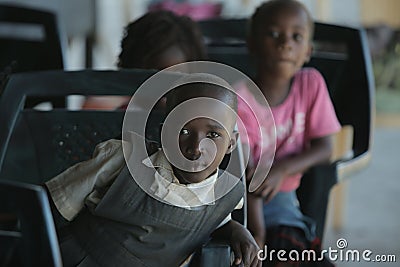 KENYA, KISUMU - MAY 23, 2017: Portrait of happy african boy sitting inside with group of children and dancing, smiling. Editorial Stock Photo