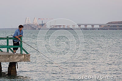 Kerch, Crimea - August 01, 2018: Woman fisherman on the pier against of the Crimean bridge Editorial Stock Photo
