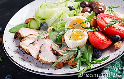 Ketogenic diet. Boiled egg, pork steak and olives, cucumber, spinach, brie cheese, nuts and tomato Stock Photo