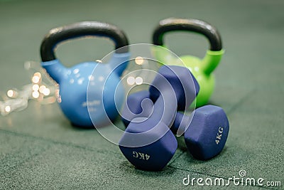 Kettle bells in a Gym. Christmas fitness composition with blue dumbbells, gift on white background with bokeh and show. Greeting Stock Photo