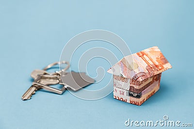 Key and house keychain on real estate with origami from russian rubles. Light blue background. Copy space. Concept of Stock Photo