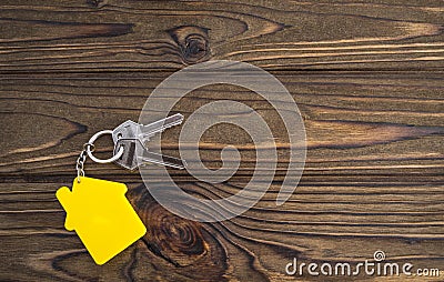 Key with yellow shaped house keychain on chain on wood texture background. Stock Photo