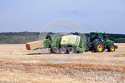 Kharkiv / Ukraine - June 27, 2019: A tractor combine harvester collects straw into bales after mowing rye wheat in an agricultural Editorial Stock Photo