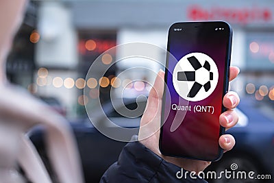 Quant QNT coin symbol. Trade with cryptocurrency, digital and virtual money, mobile banking. Hand with smartphone Editorial Stock Photo