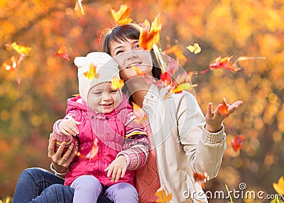 Kid and beautiful mother play and throw leaves outdoor in autumn Stock Photo