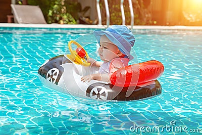 Kid behind the wheel in the pool. Summer vacation at sea. A little girl less than one year old is driving an inflatable boat in Stock Photo