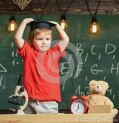 Kid boy in graduate cap ready to go to school, chalkboard on background. Kindergarten graduation concept. First former Stock Photo