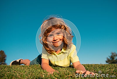 Kid boy laying on the green grass. Happy child playing in green spring field against sky background. Freedom kids and Stock Photo