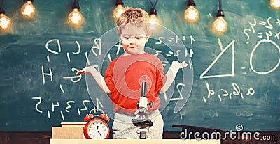 Kid boy near microscope, clock in classroom, chalkboard on background. First former confused with studying, learning Stock Photo