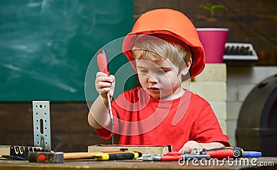 Kid boy in orange hard hat or helmet, study room background. Little helper concept. Boy play as builder or repairer Stock Photo