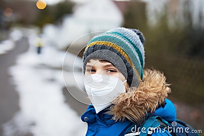 Kid boy wearing ffp medical mask on the way to school. Child backpack satchel. Schoolkid on cold autumn or winter day Stock Photo