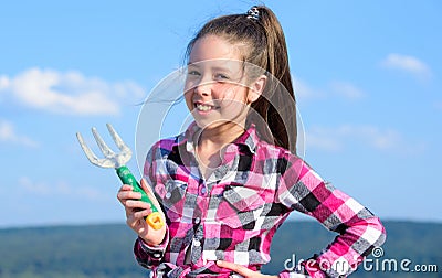 Kid cheerful gardener hold rake blue sky background. Girl gardener with hand rake. Gardening and harvesting concept Stock Photo