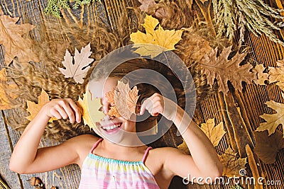 Kid cute girl play with leaves wooden background top view. Child long hair play with dry leaves. Autumn coziness is just Stock Photo