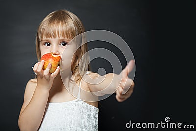 Kid eating fresh red apple happy and doing ok sign, thumb up with fingers, excellent sign Stock Photo