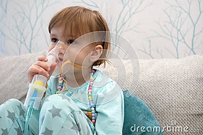 Kid girl makes inhalation with a nebulizer. sick child holding inhalator in hand and breathes through an inhaler at home Stock Photo