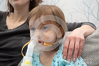 Kid girl makes inhalation with a nebulizer. sick child with mother holding inhalator in hand and breathes through an inhaler at Stock Photo