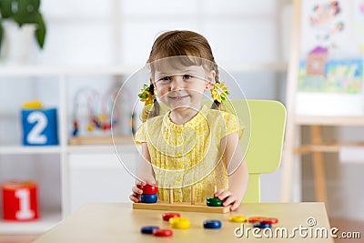 Kid girl playing with logical toy on desk in nursery room or kindergarten. Child arranging and sorting colors and sizes Stock Photo