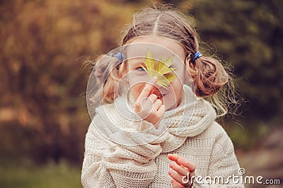 Kid girl walking in the garden in late october or november and playing with maple leaf. Children exploring nature Stock Photo