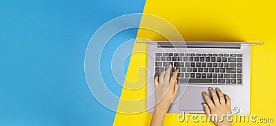 Kid hands typing on laptop computer keyboard, top view, yellow and blue background Stock Photo