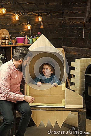 Kid happy sit in cardboard hand made rocket. Child boy play cosmonaut, astronaut. Parenthood concept. Boy play with dad Stock Photo