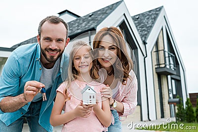 Kid holding carton house model near father with keys and happy mother Stock Photo