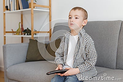 Kid holding TV remote controller. Boy without parental control watching television Stock Photo