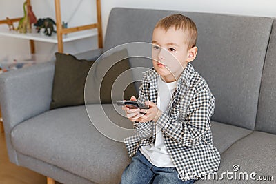 Kid holding TV remote controller. Boy without parental control watching television Stock Photo